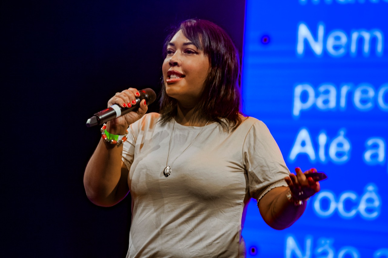 Dani Monteiro falando em um palco com microfone